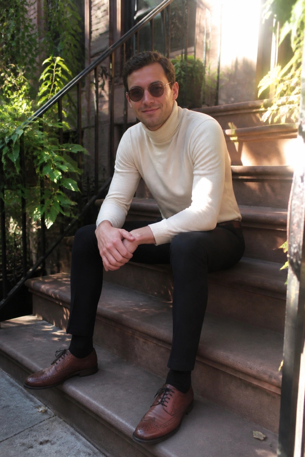 Man in cream turtleneck, black pants, and brown brogues on stone steps