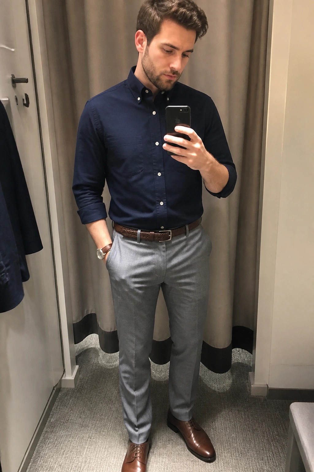 Man in navy shirt and gray pants taking mirror selfie in dressing room