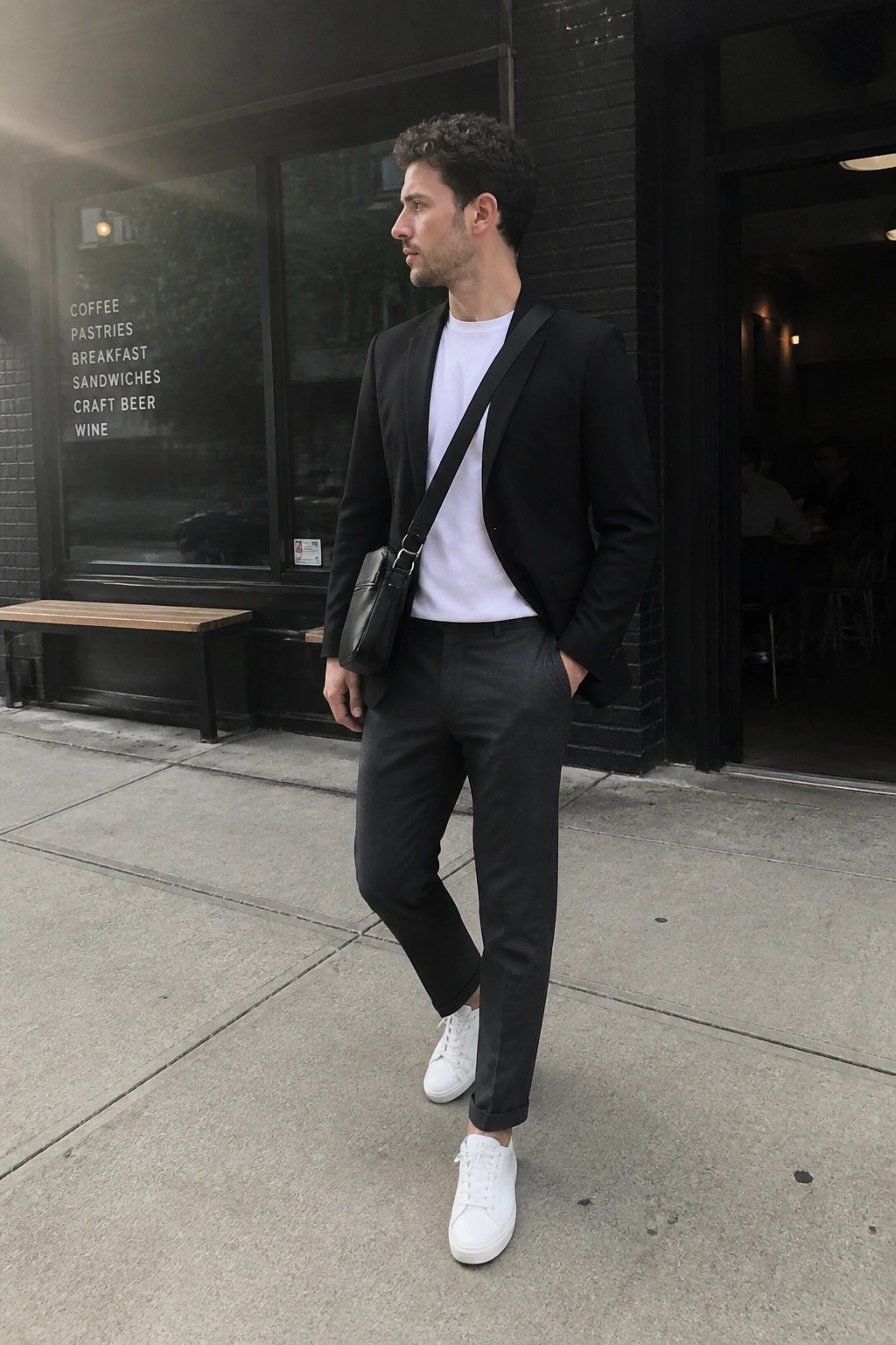 Man in black blazer over white t-shirt with crossbody bag outside cafe window
