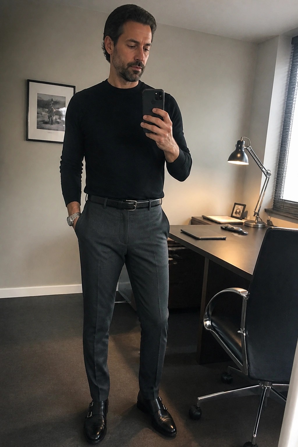 Man in black sweater and gray trousers taking selfie in office