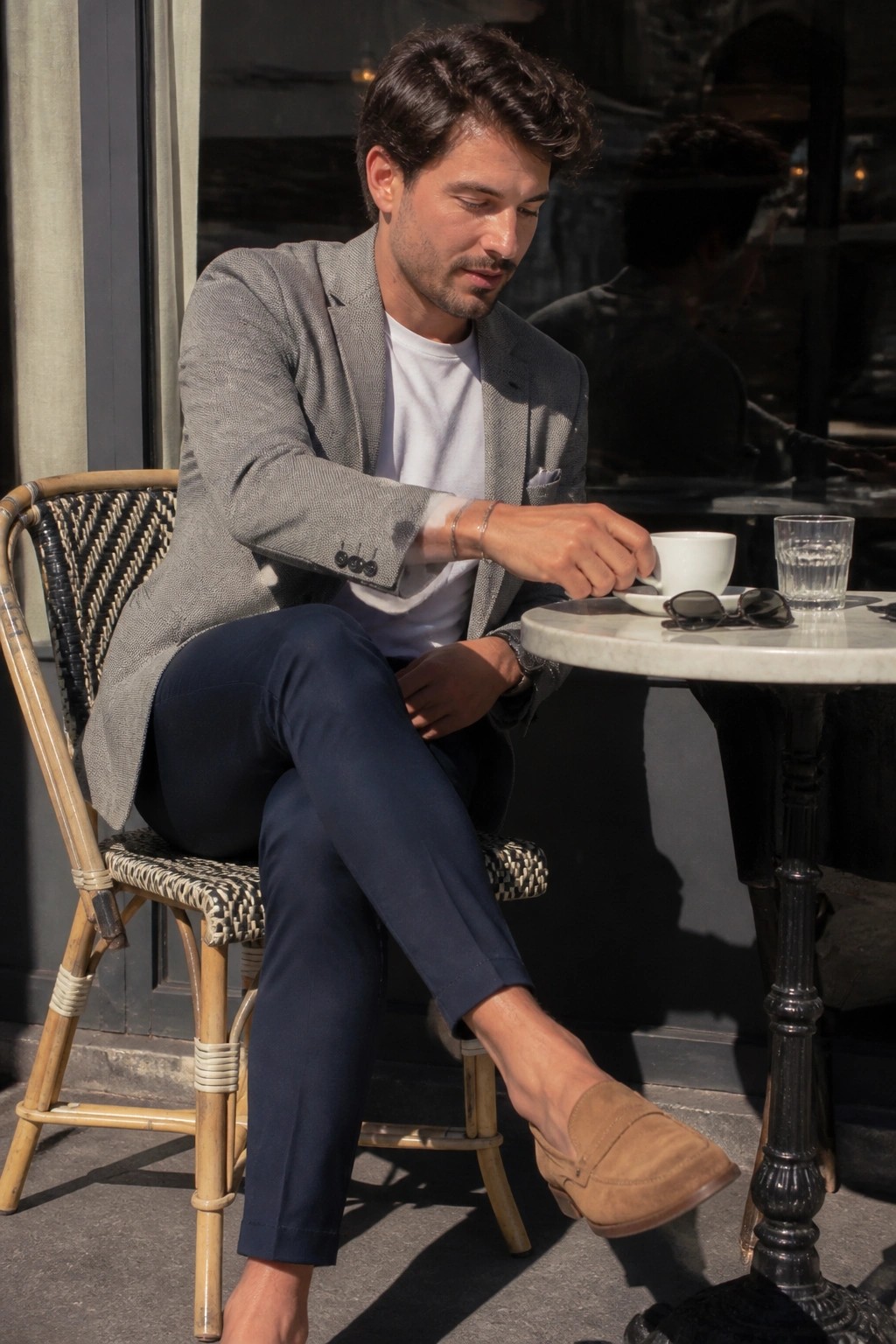 Man in gray blazer sipping coffee at sunny outdoor cafe table.
