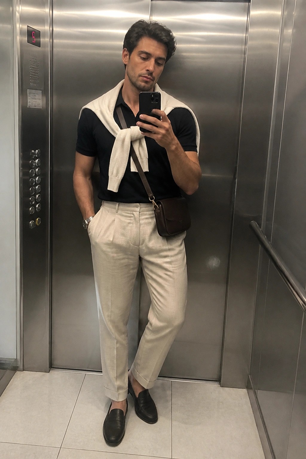 Man in black polo with white sweater over shoulders in elevator taking selfie