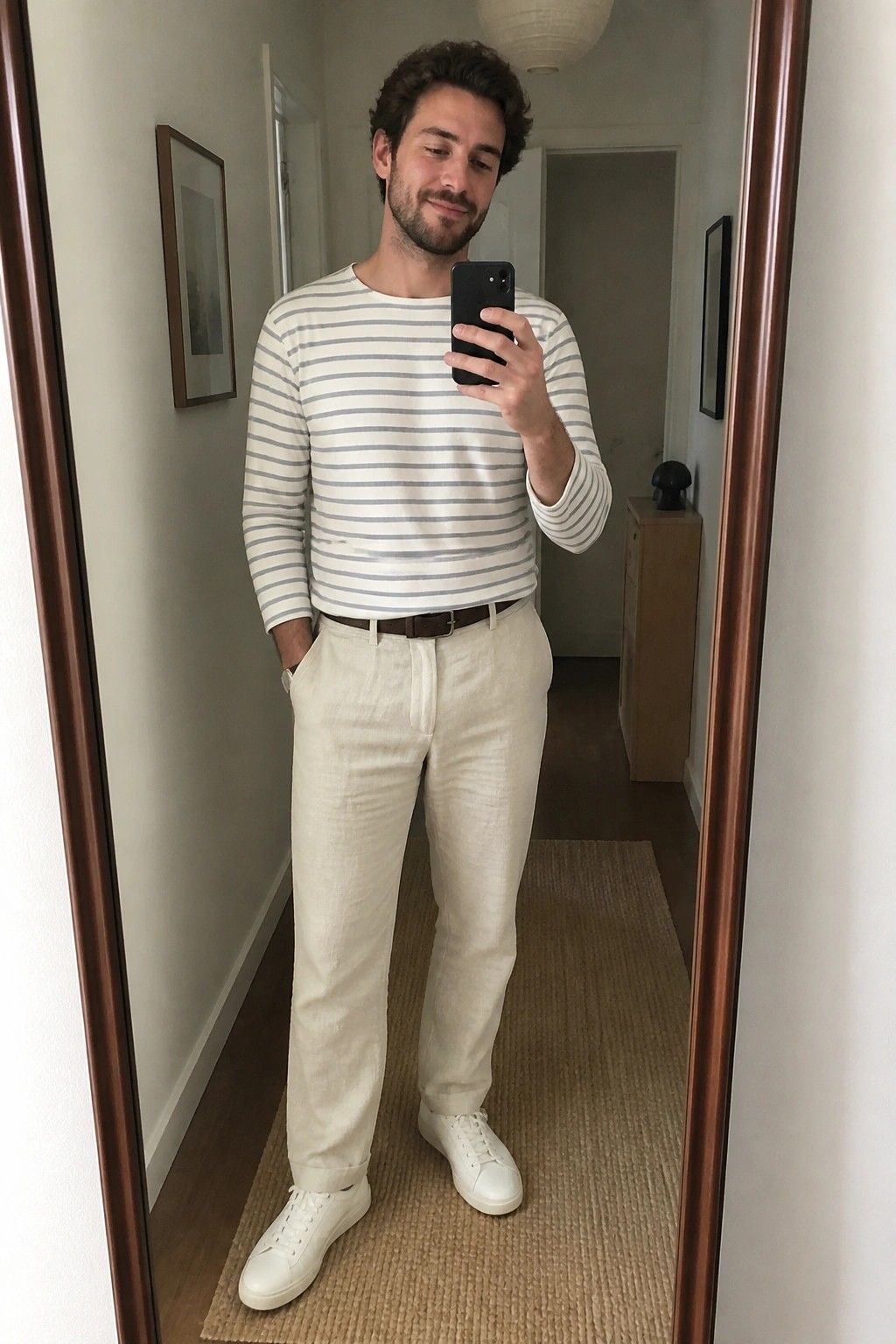 Man in striped shirt and beige pants taking mirror selfie in hallway