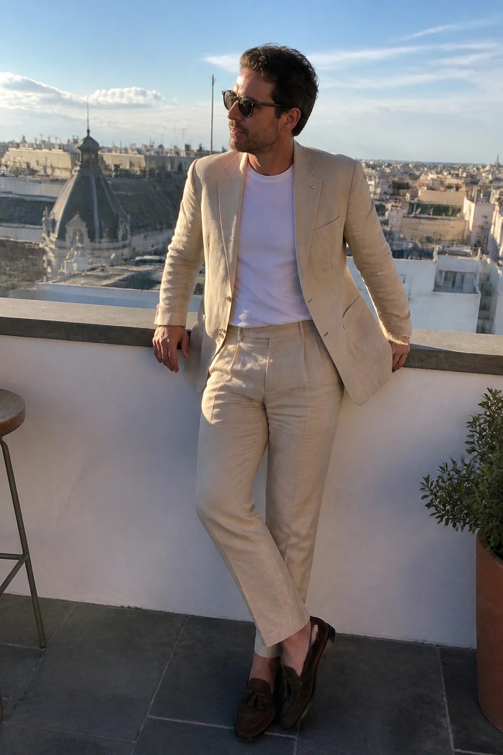 Man in beige linen pants and matching blazer over a white tee with brown suede tassel loafers standing outdoors.