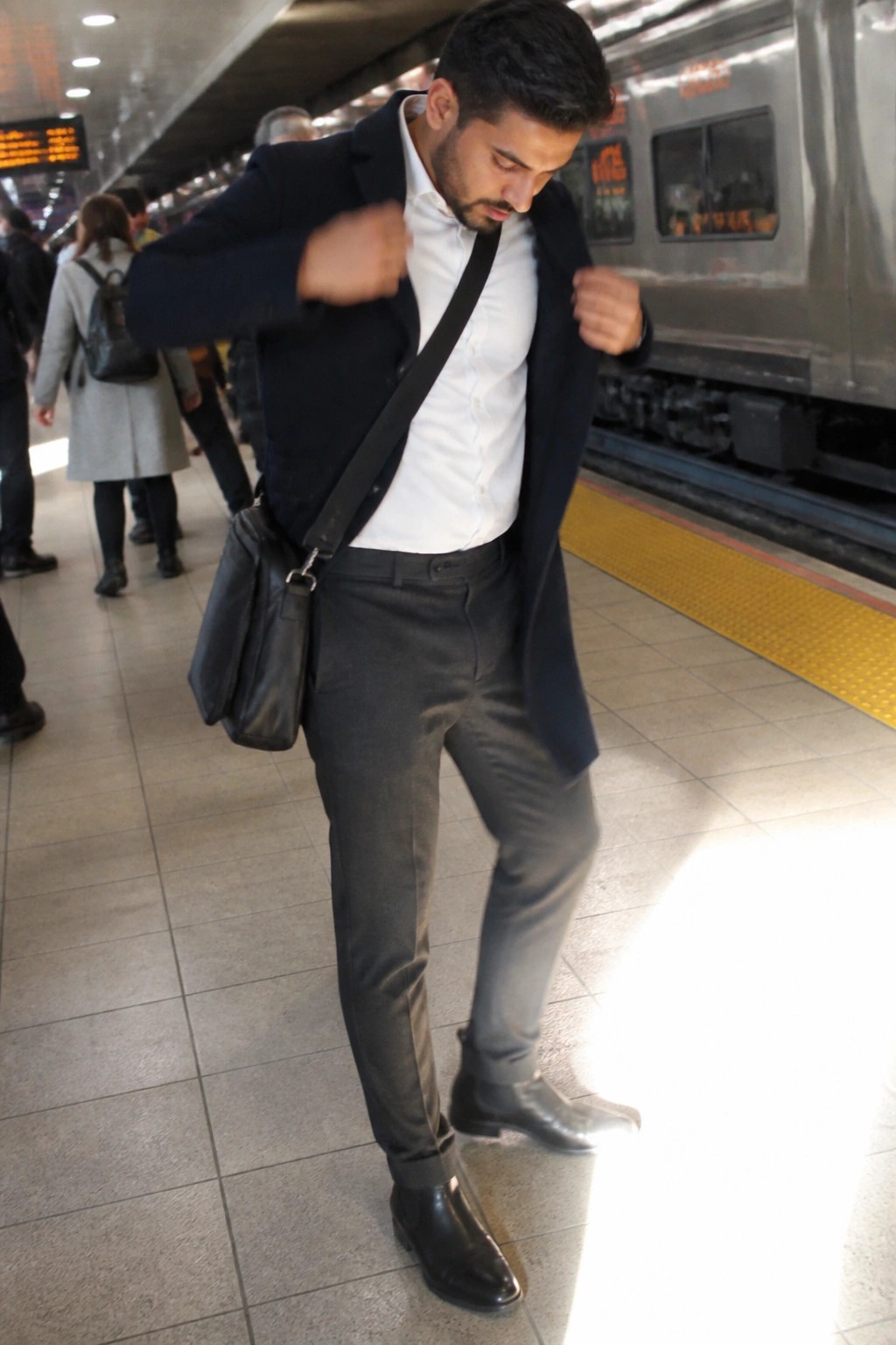Man adjusting navy blazer over white shirt on subway platform