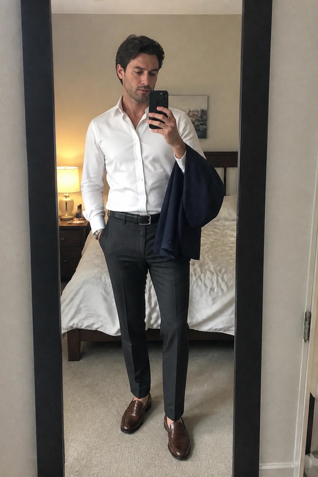 Man in white shirt and gray pants holding navy blazer for mirror selfie