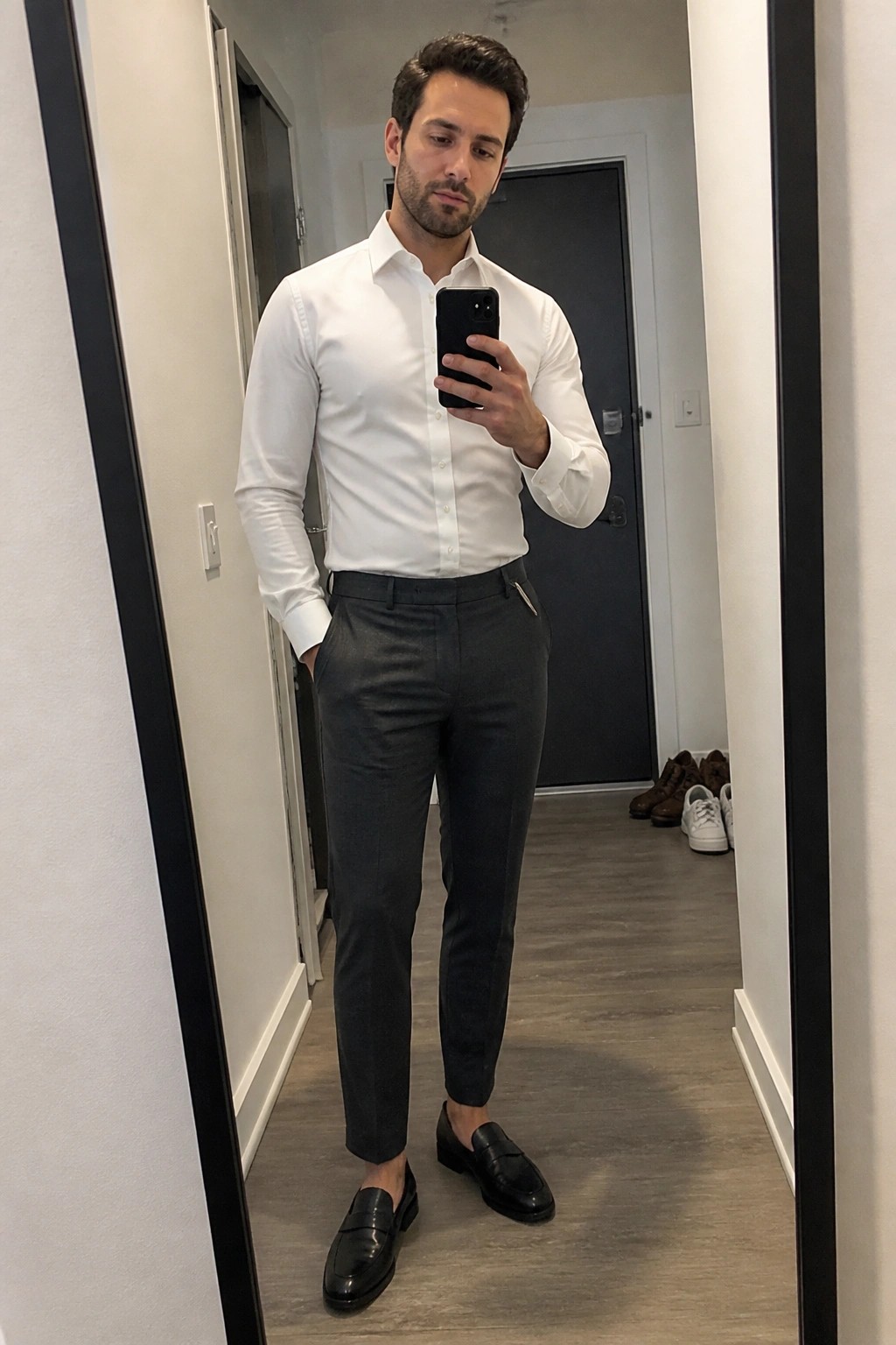 Man in white shirt and gray pants taking mirror selfie in hallway