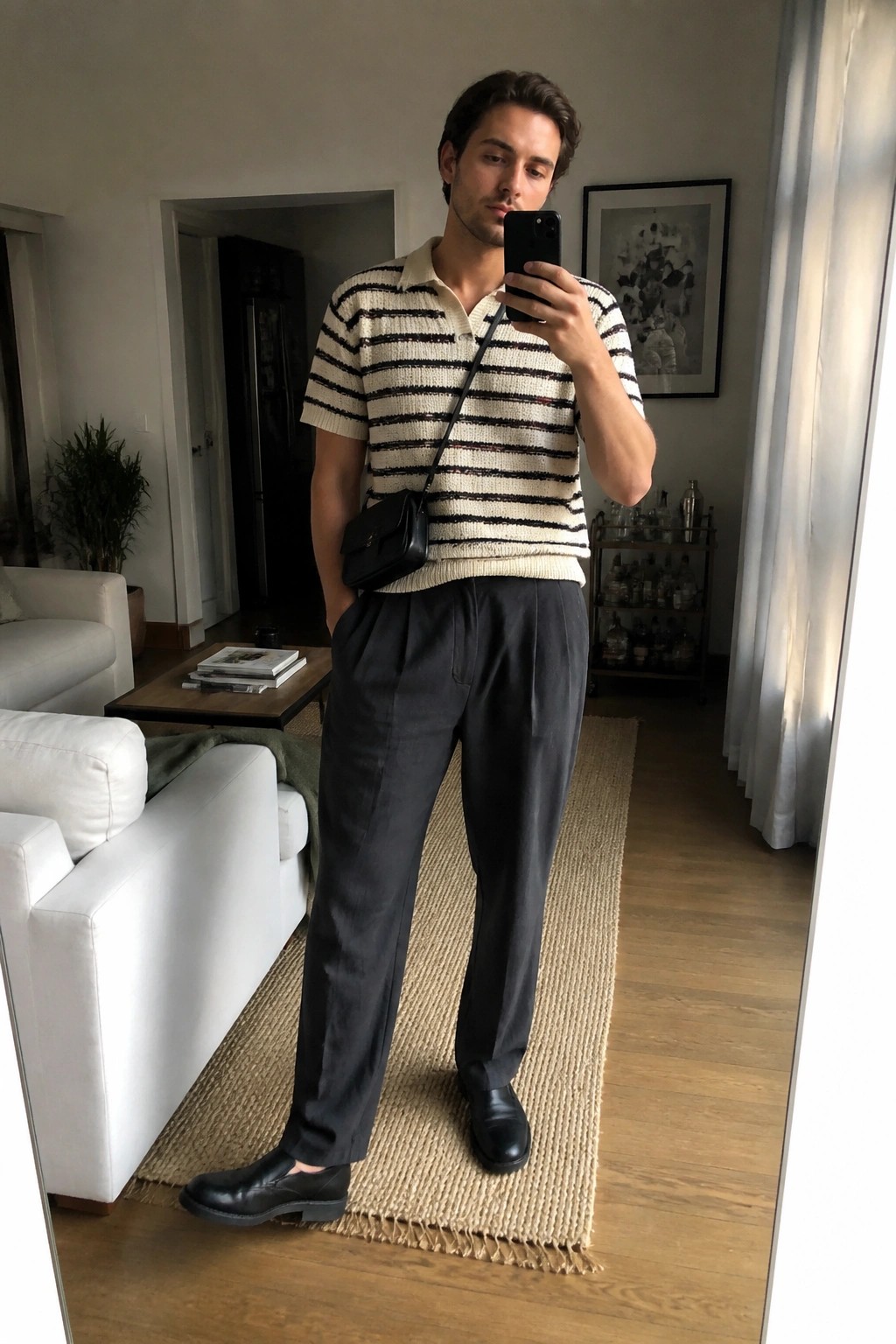 Man in striped polo shirt and gray trousers taking mirror selfie in living room