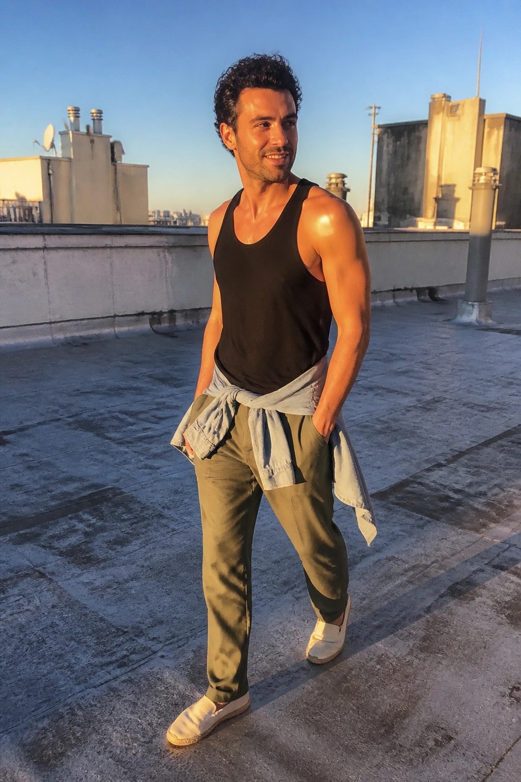 Muscular man in black tank top with tied denim shirt on rooftop