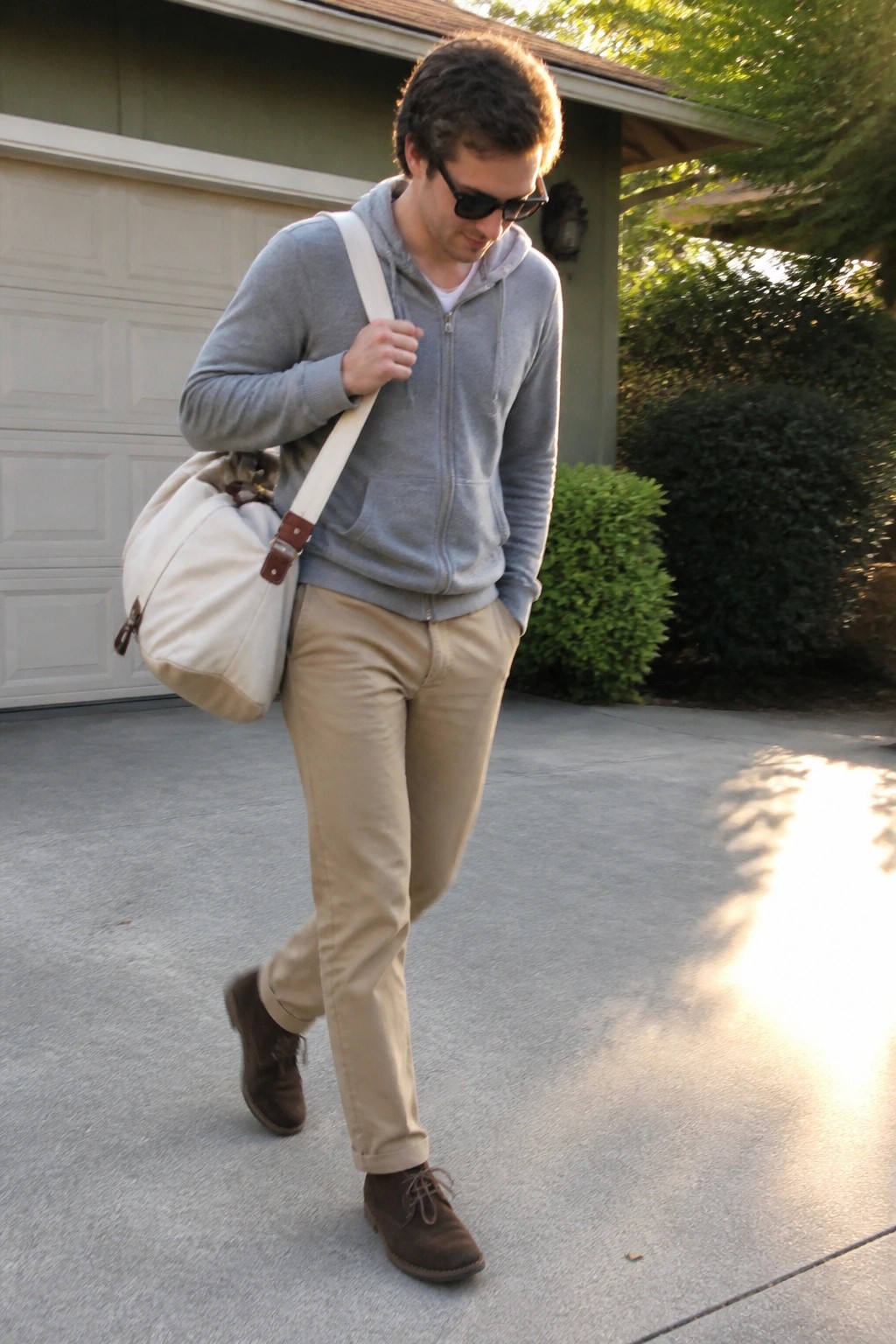 Man in gray hoodie carrying cat inside white duffel bag on driveway