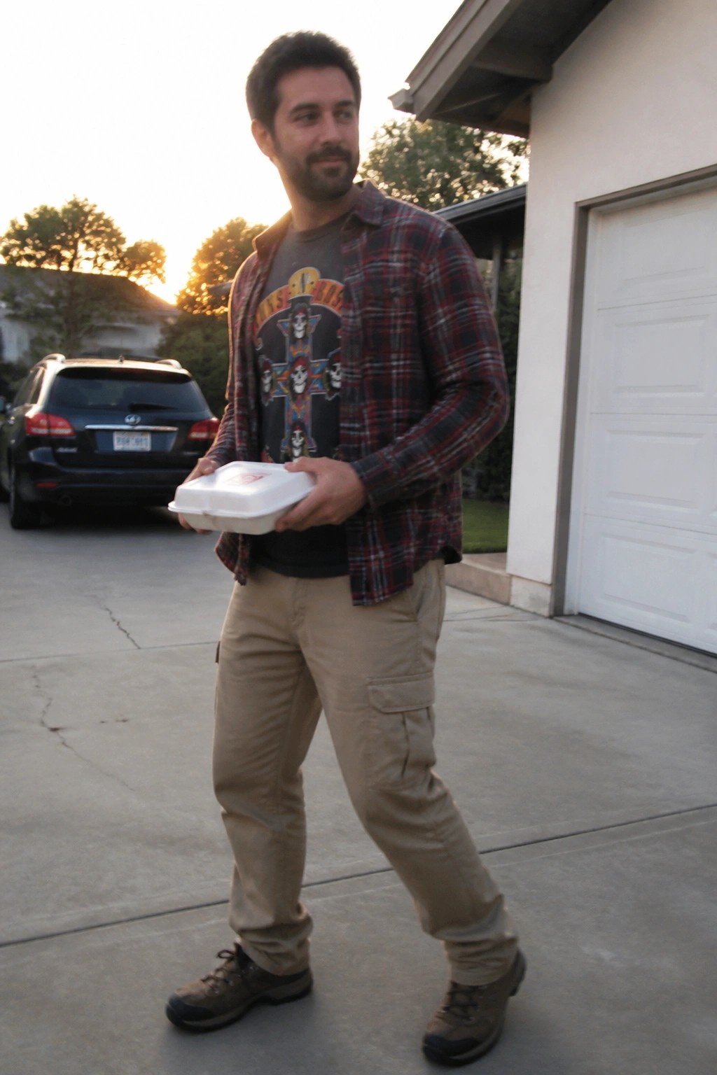 Man in red plaid shirt holds white takeout container on driveway at sunset