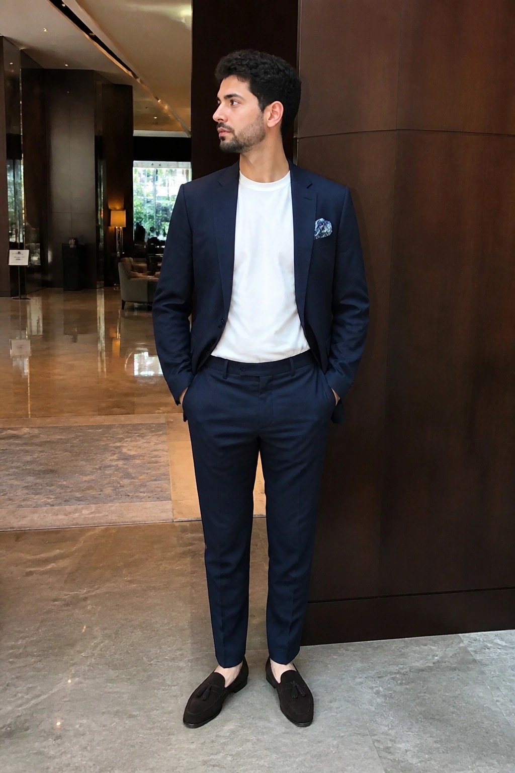 Man in navy suit and white t-shirt with brown loafers in marble lobby