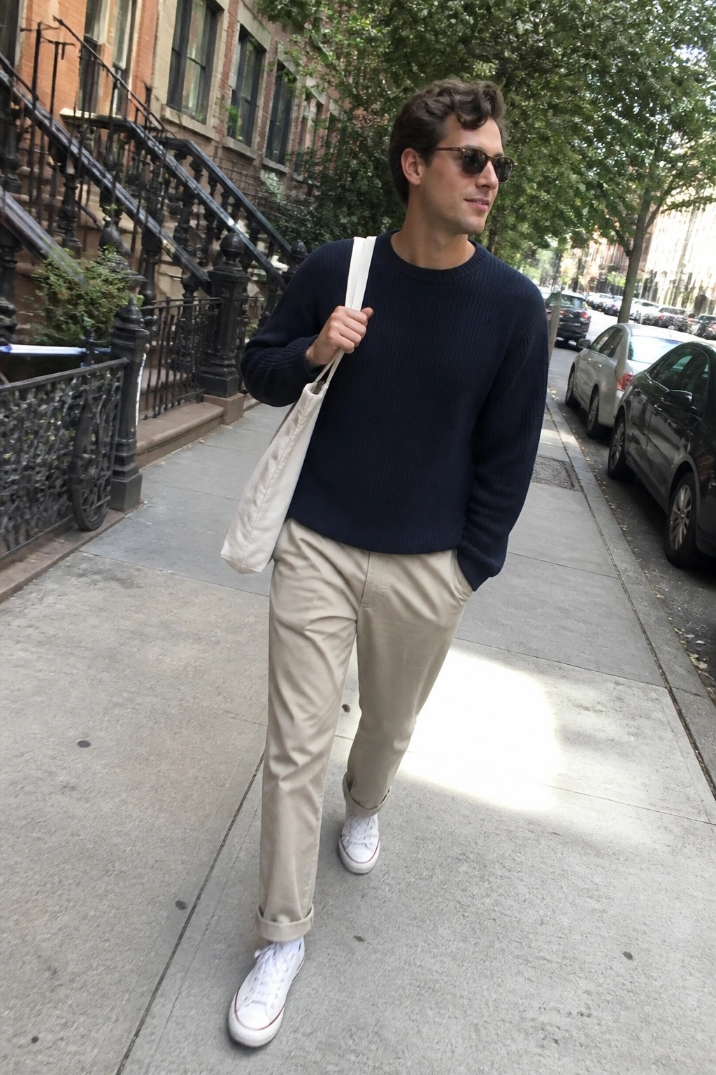 Man in navy sweater and beige pants with tote bag on city sidewalk