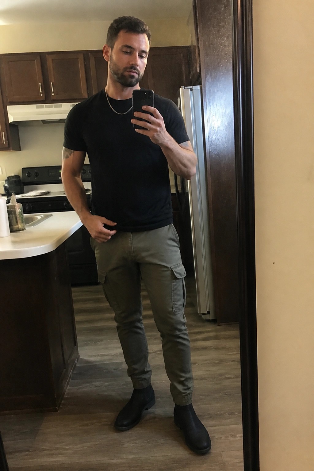 Bearded man in black t-shirt and olive cargo pants taking mirror selfie.