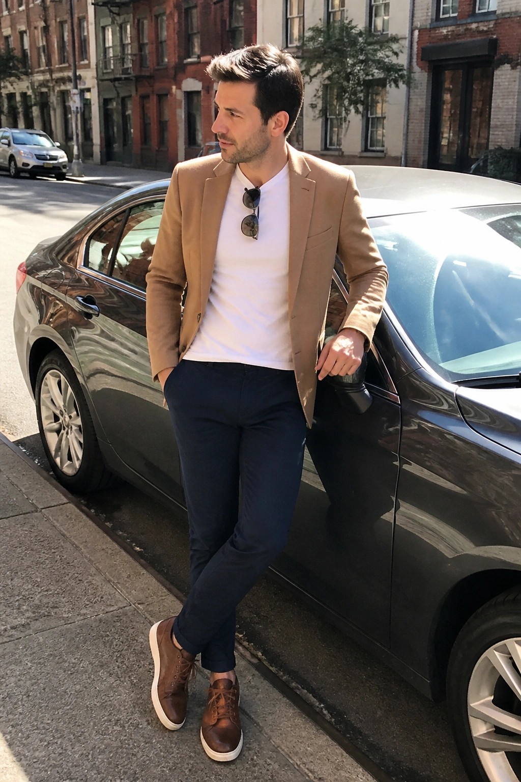 Man in tan blazer and white tee leaning against black car on city street