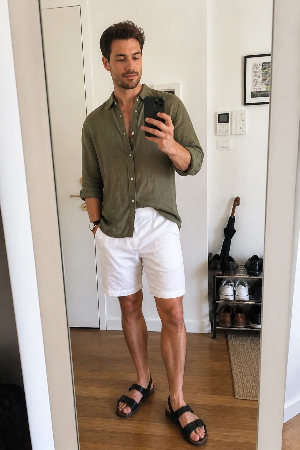 Man in olive shirt and white shorts taking mirror selfie with phone