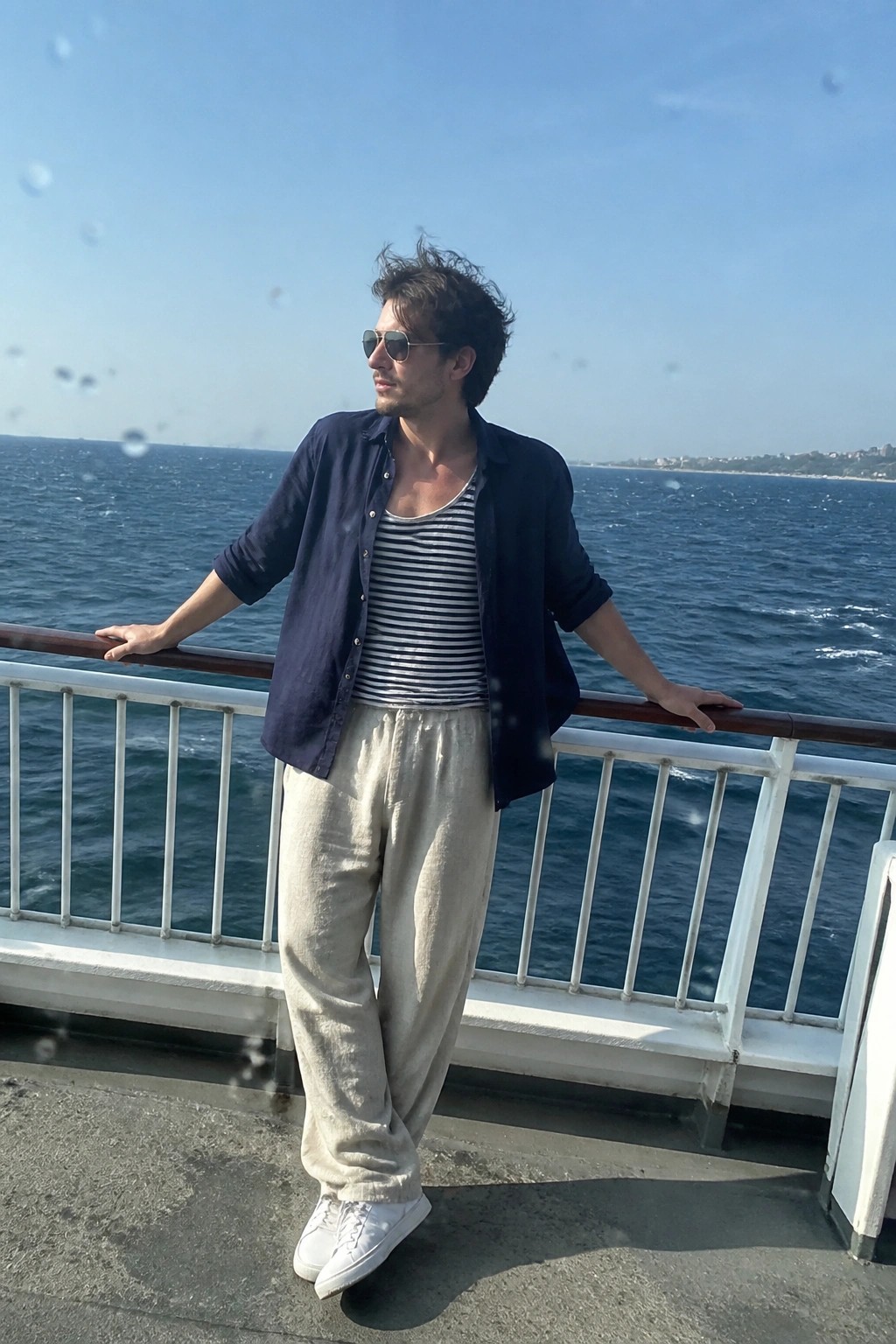 Man in blue shirt over striped tank top on boat railing by sea