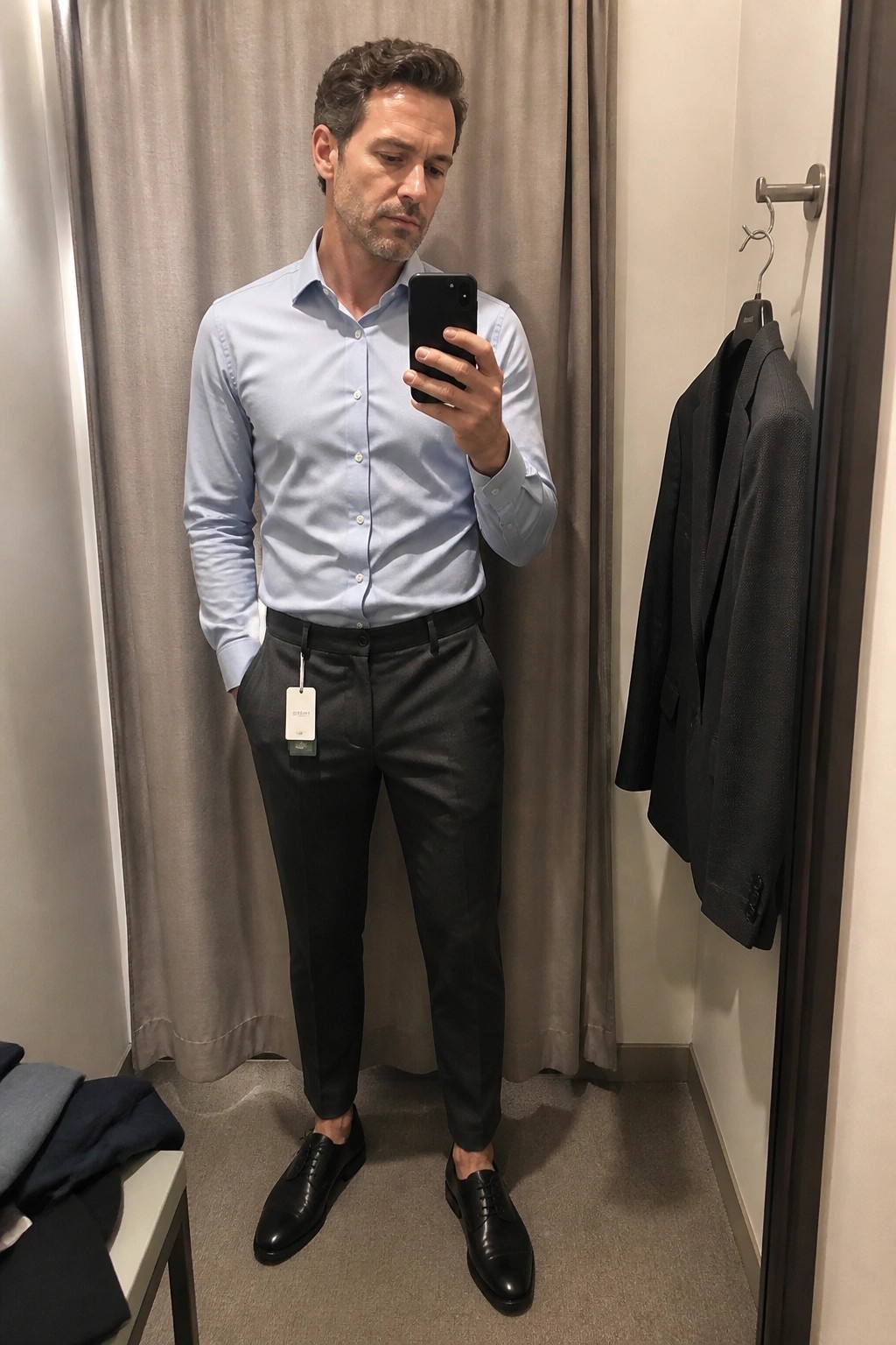 Man in light blue shirt and gray pants taking mirror selfie in fitting room