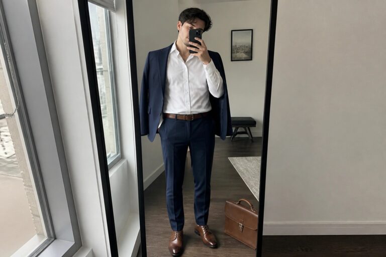 Man in navy suit with white shirt taking mirror selfie holding phone