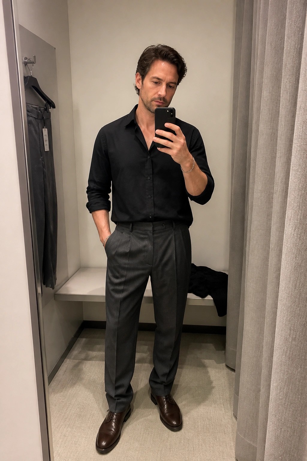 Man taking mirror selfie in black shirt and gray trousers in fitting room
