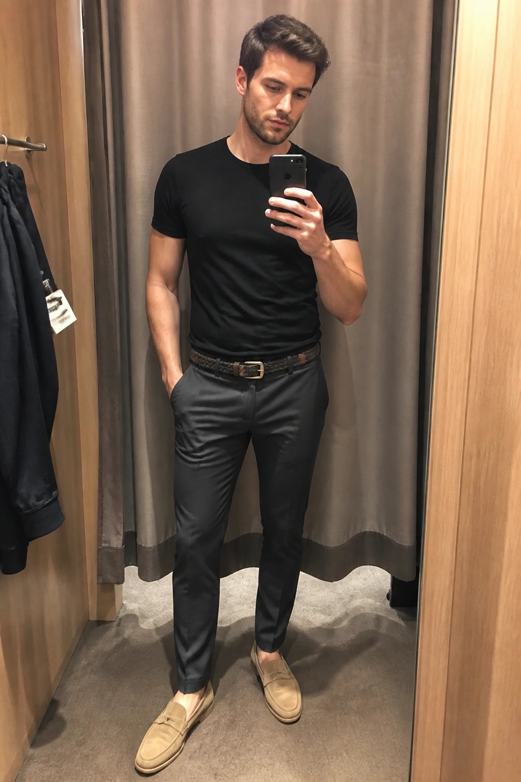 Man in black t-shirt and gray pants taking mirror selfie in fitting room