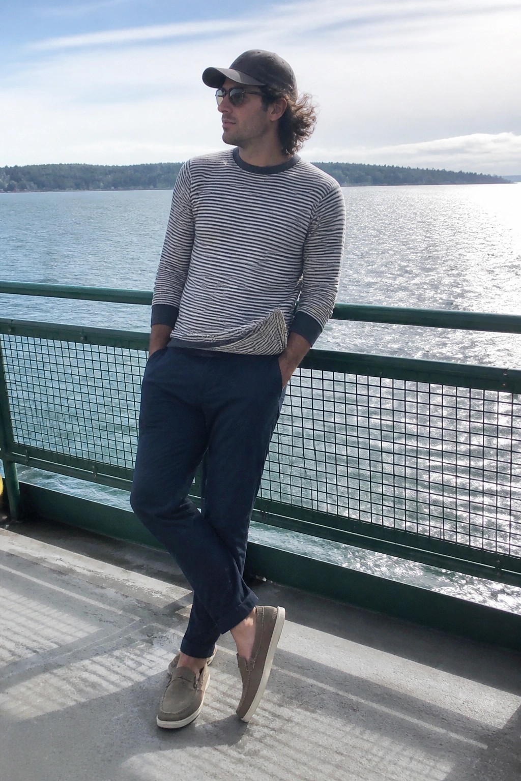 Man in striped shirt and cap leaning on green boat railing by water.