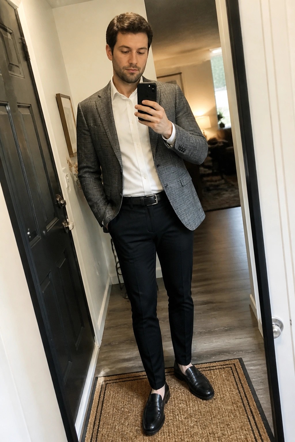 Man in gray plaid blazer, white shirt, black pants, and loafers holds phone