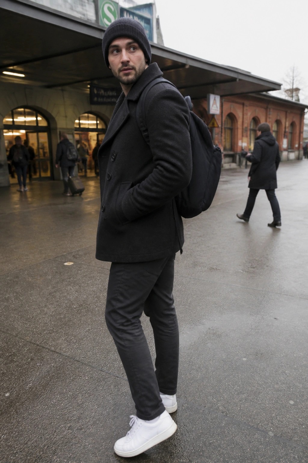 Man in dark coat and beanie with backpack at train station
