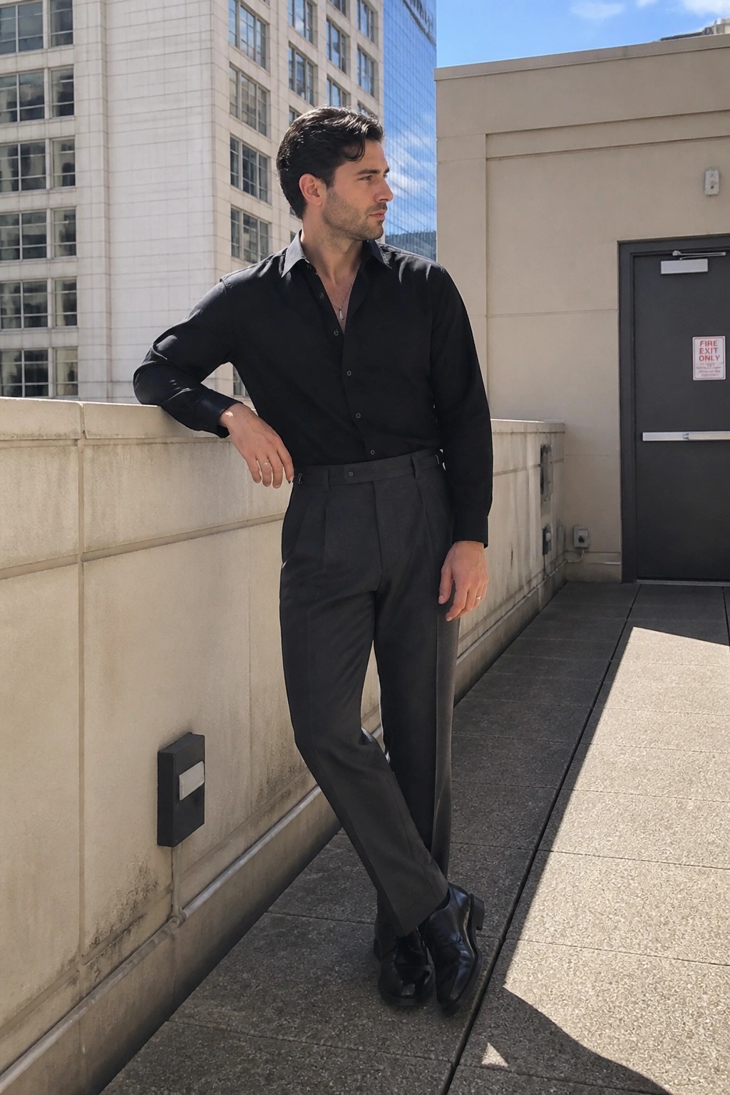 Man in black shirt and gray pleated trousers leaning on sunny rooftop ledge