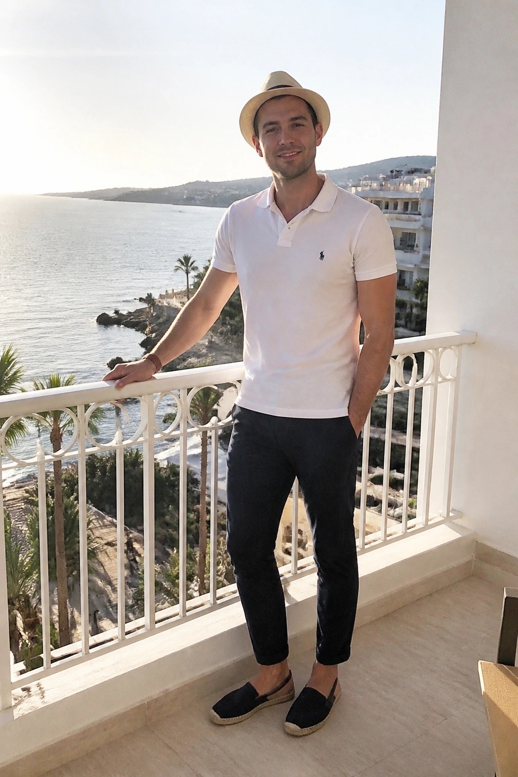 Man in white polo shirt and hat on balcony overlooking the sea