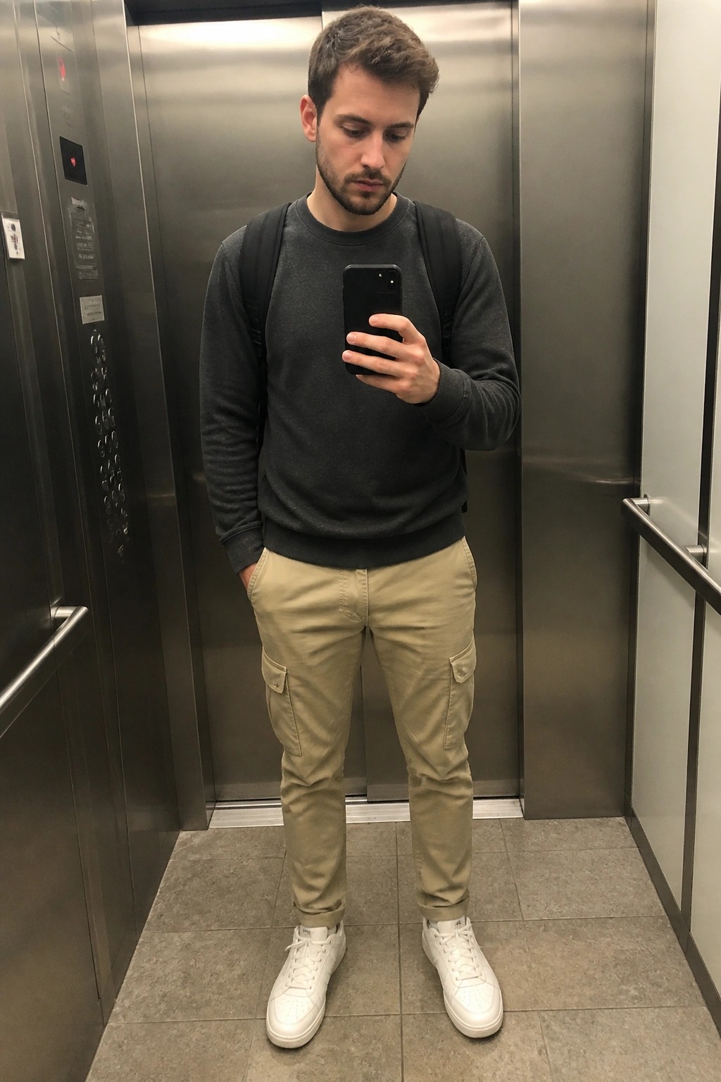 Man in gray sweatshirt and khaki cargo pants taking elevator selfie