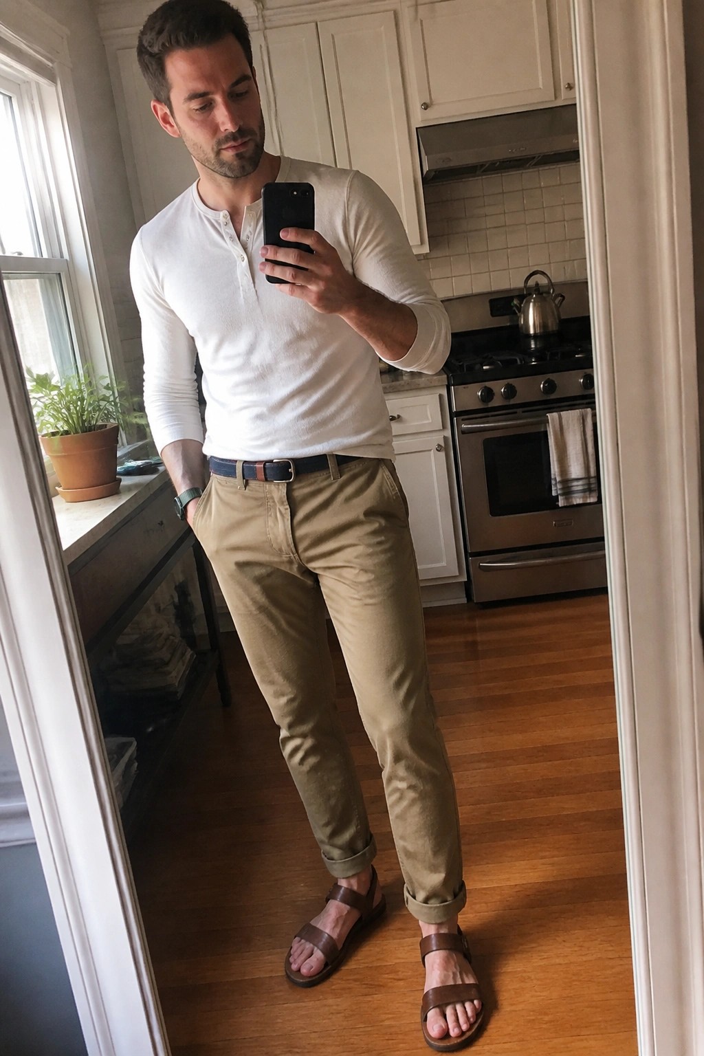Man in white henley and khaki pants taking mirror selfie in kitchen
