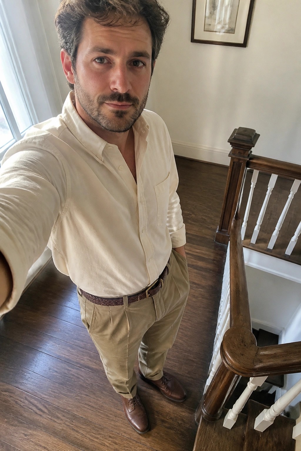 Man in cream shirt and khaki pants taking selfie near wooden staircase