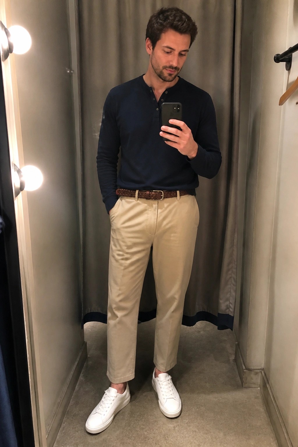 Man in navy henley, khaki pants, braided belt, white sneakers taking mirror selfie