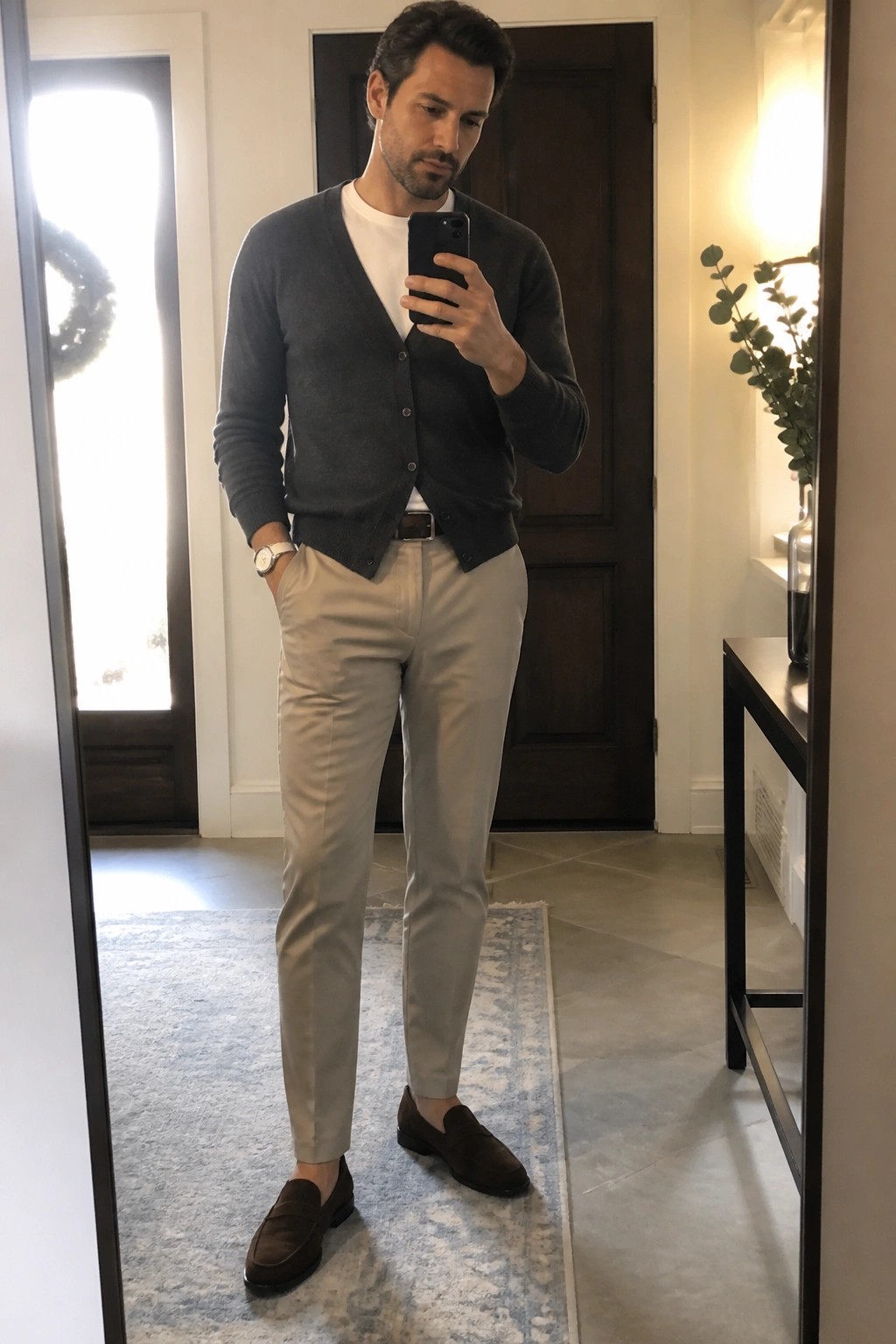 Man in gray cardigan, white tee, beige pants, and brown loafers taking mirror selfie.
