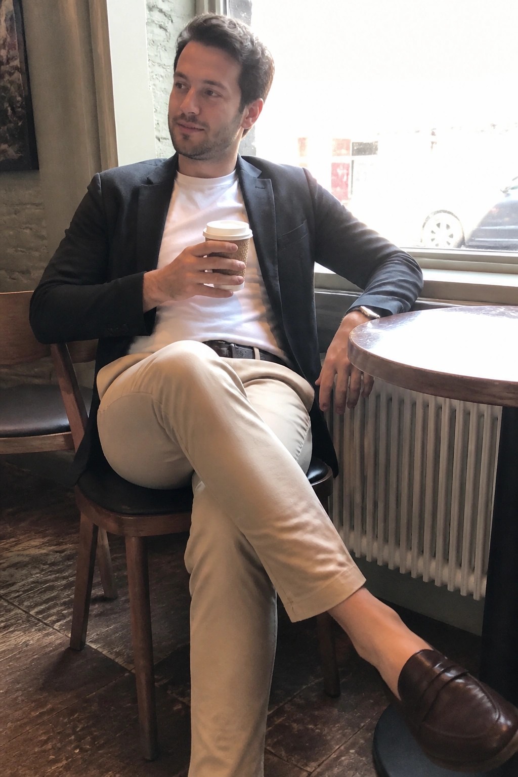 Man in dark blazer and beige pants holding coffee cup in cafe.