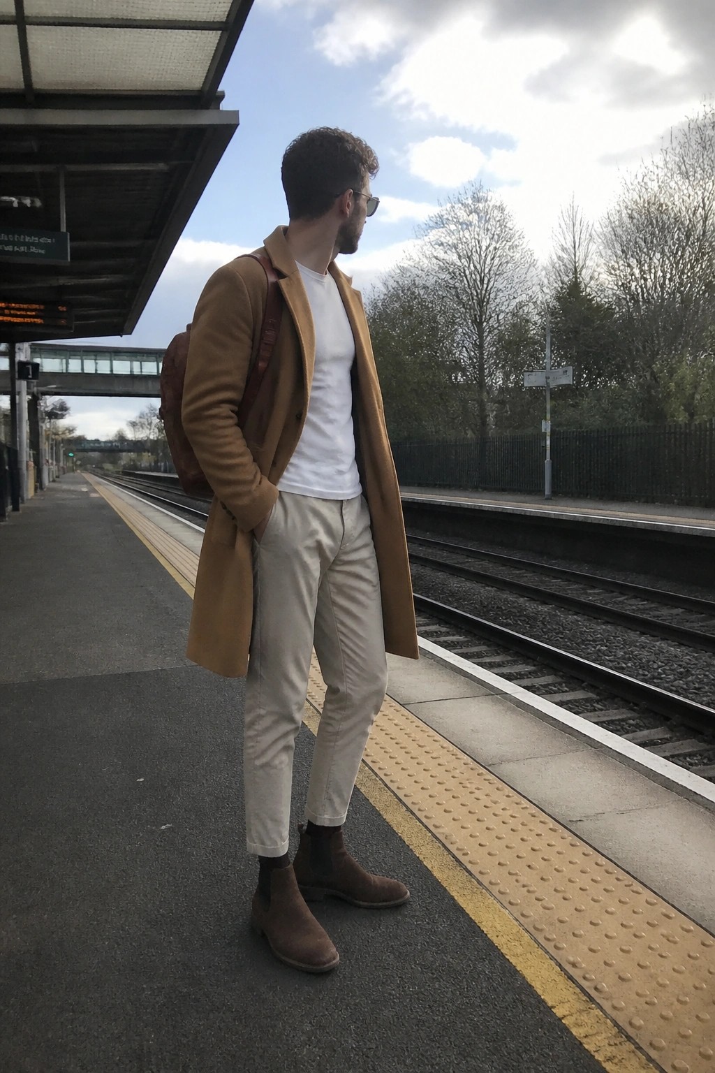 Man in tan coat and white shirt on train platform with backpack