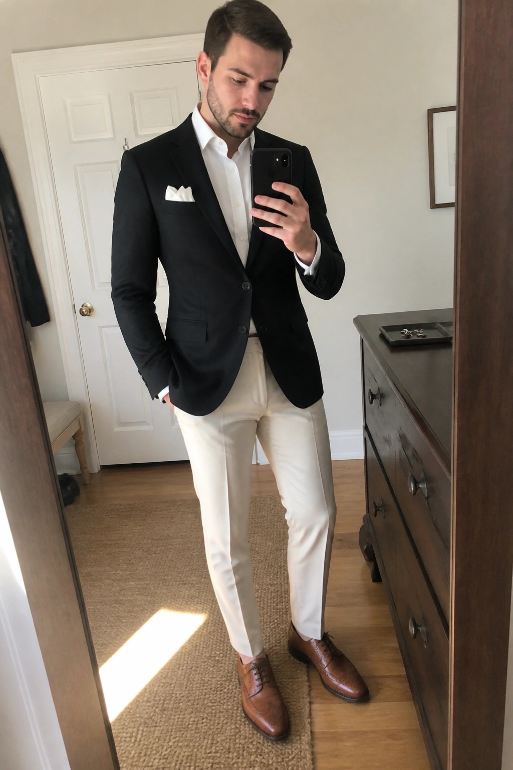 Man in black blazer, white shirt, cream pants taking mirror selfie