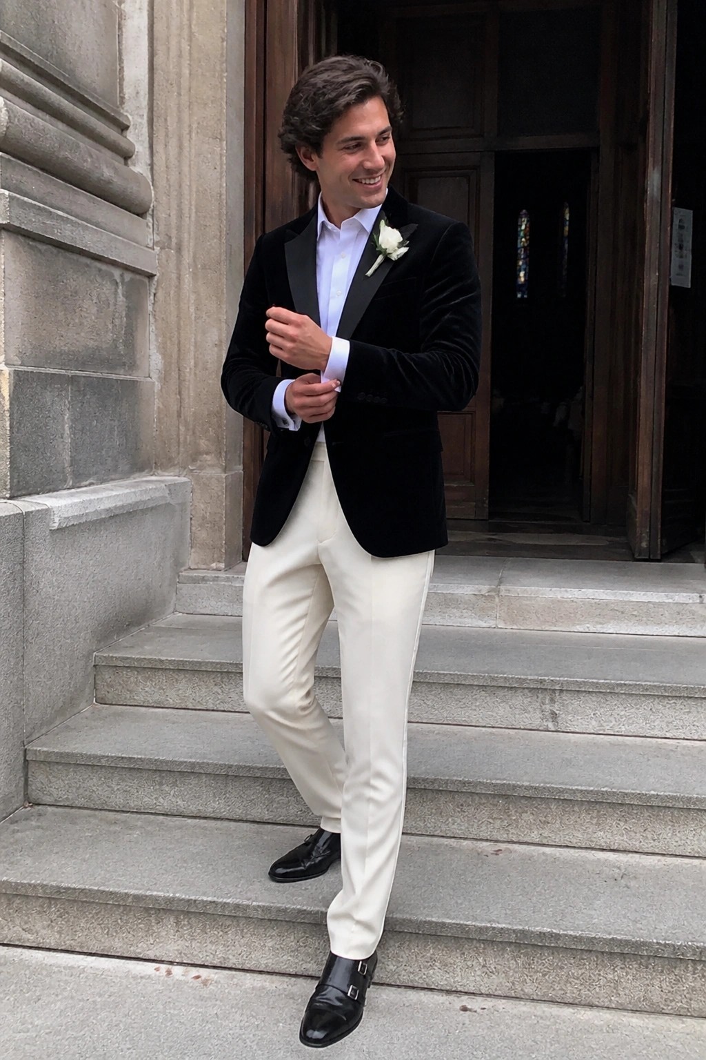 Man in black velvet tuxedo jacket and white trousers on stone steps