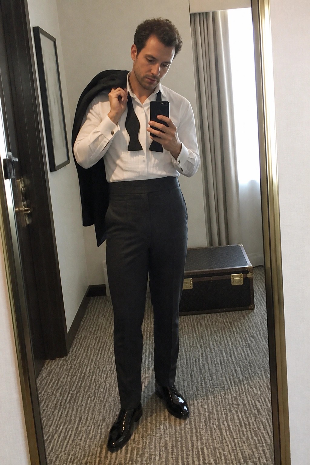 Man in white shirt taking mirror selfie with untied black bow tie and jacket