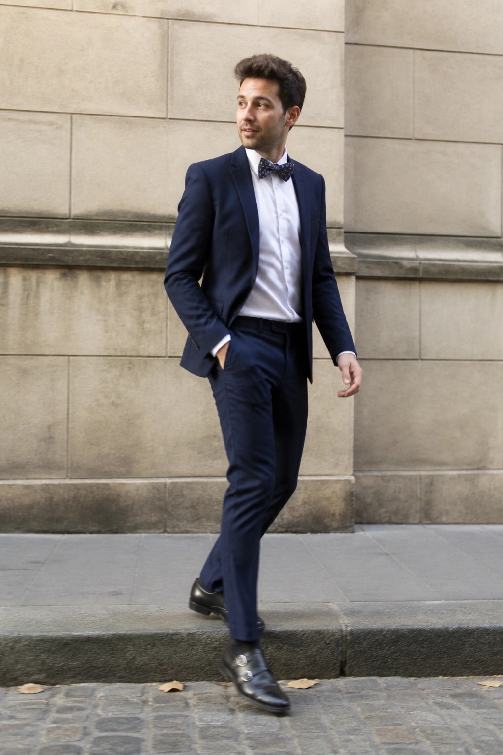 Man in navy suit and bow tie posing on stone steps with hand in pocket