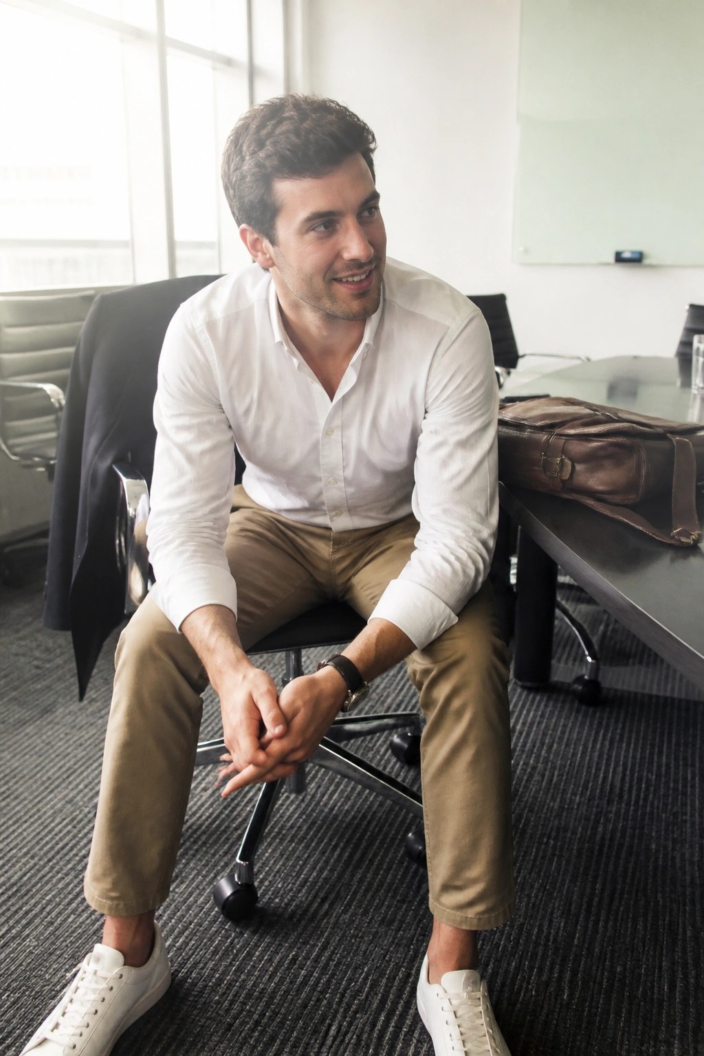 Man in white shirt and khaki pants sitting in office with hands clasped