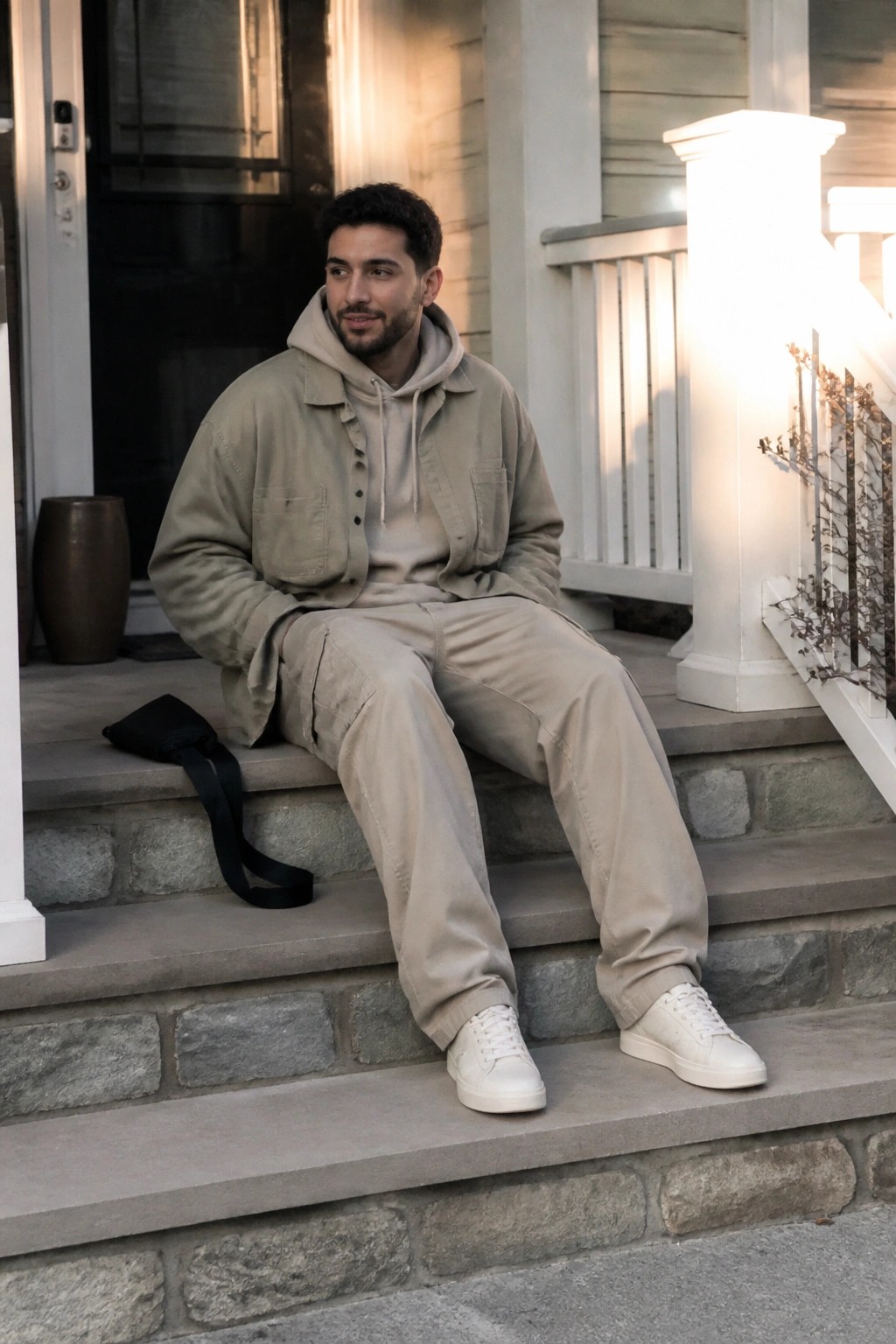 Man in beige cargo jacket and pants seated on stone porch steps
