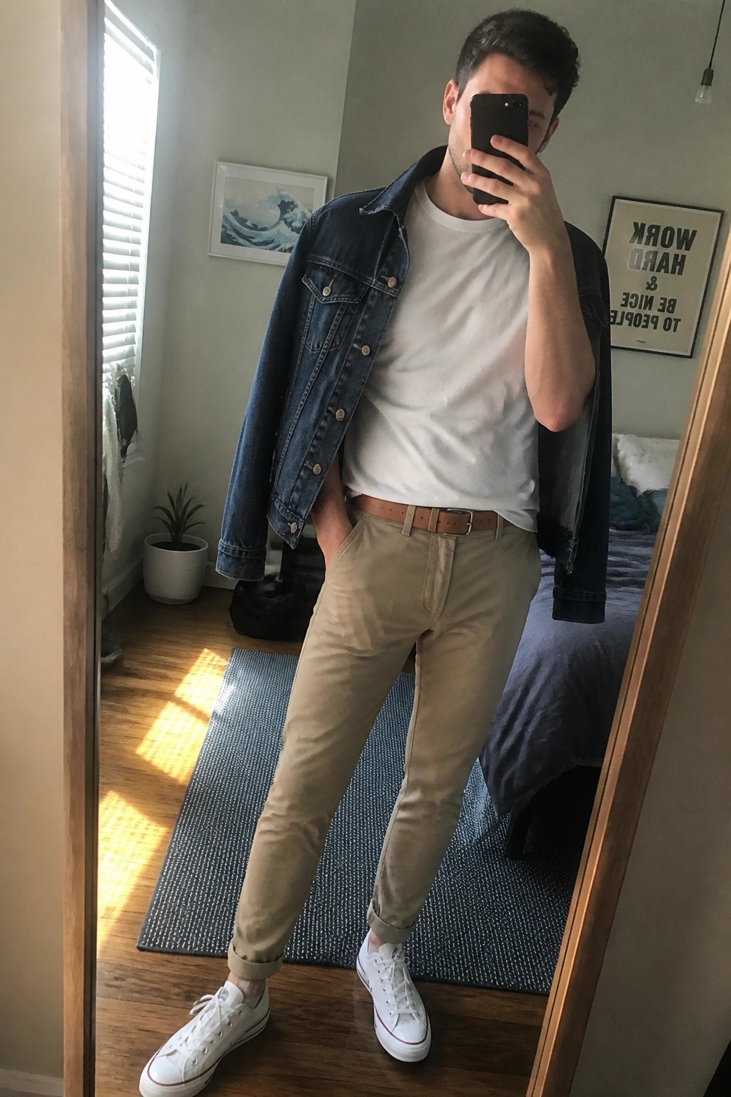 Man in denim jacket, white tee, and khakis taking bedroom mirror selfie