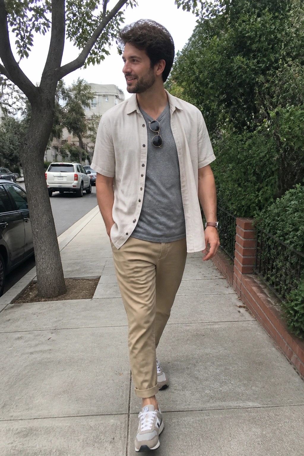 Man in beige shirt and khaki pants walking on city sidewalk