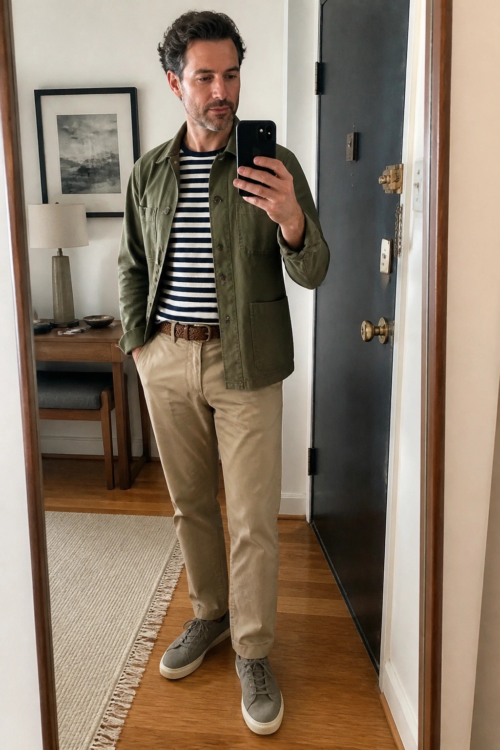 Man in green jacket over striped shirt taking mirror selfie with phone