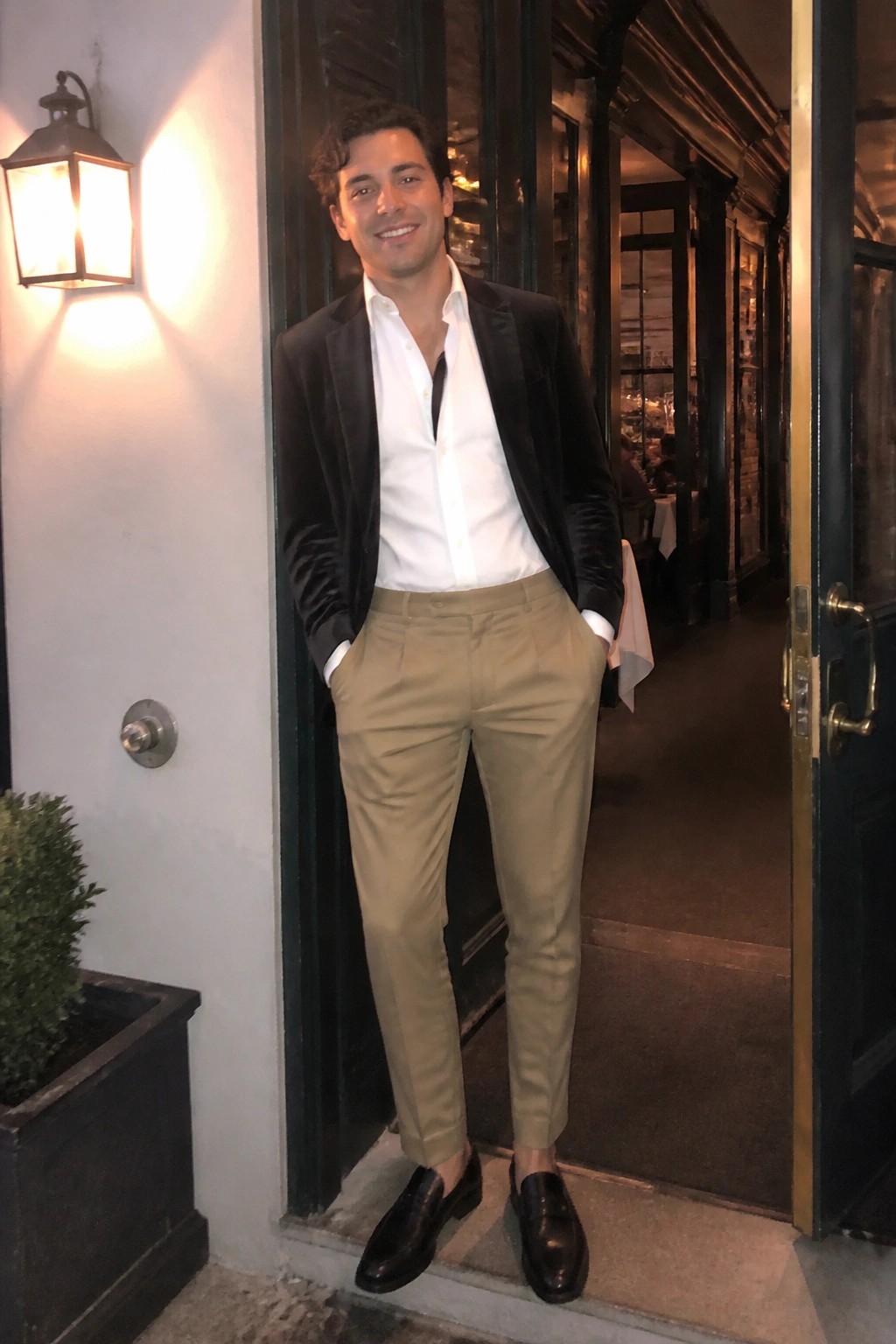 Man in black velvet blazer and khaki pants standing in open doorway