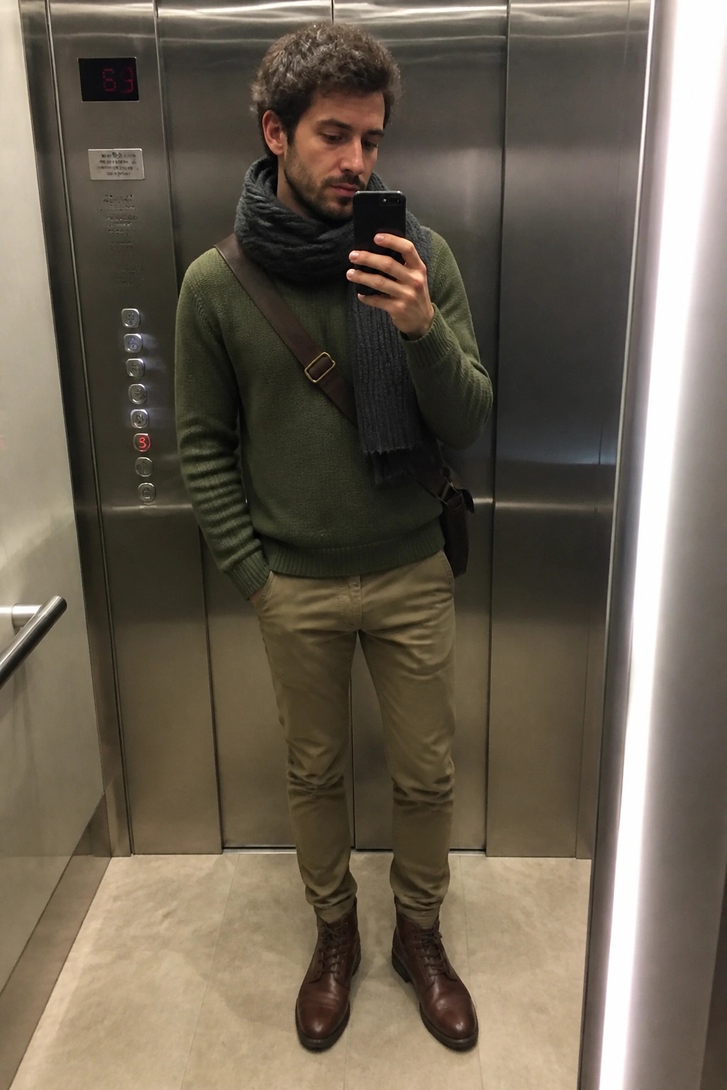 Man in green sweater and gray scarf taking selfie in elevator