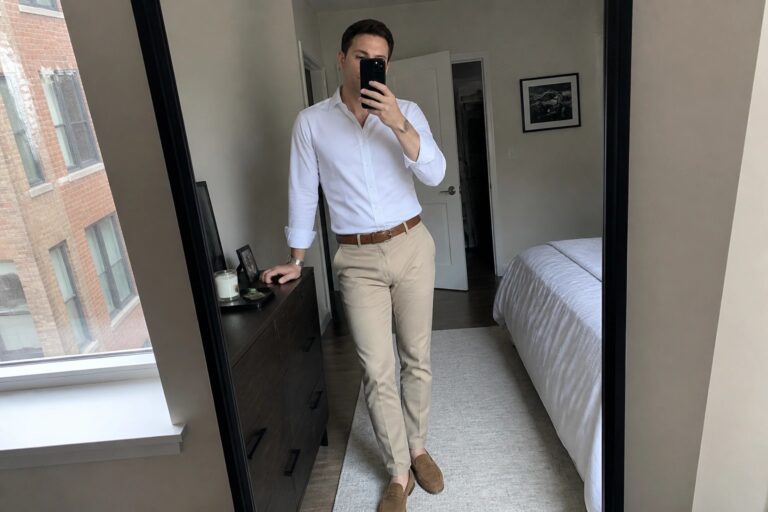20 Classic White Shirt and Khaki Pants Outfits for Men That Always Look Put Together Man wearing a white button down shirt tucked into khaki pants with a brown belt and brown suede loafers while holding a phone in a mirror selfie.