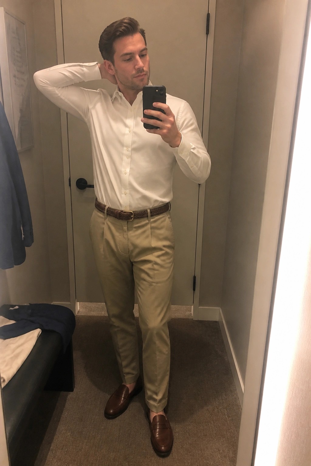Man in white shirt and khaki pants taking mirror selfie in fitting room